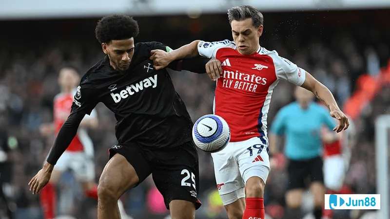 Cầu thủ Arsenal với chiếc áo đỏ đang vượt qua hậu vệ của West Ham trên sân cỏ Cầu thủ Arsenal với chiếc áo đỏ đang vượt qua hậu vệ của West Ham trên sân cỏ